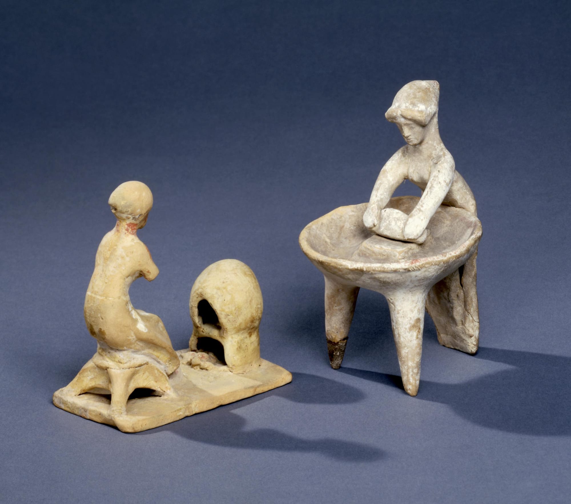 Two terracotta figures from ancient Greece (Boeotia) showing them baking bread at a dome shaped clay oven and the other, kneading bread. 500 BC