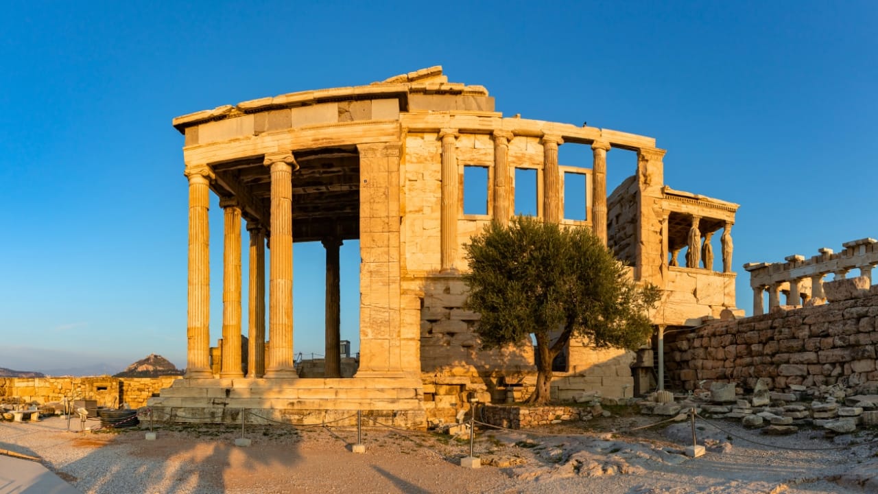 The Acropolis of Athens showing the sacred olive tree, the Erechtheion, part of the Parthenon and the city of Athens with Mt. Lycavitos and Mt. Pendeli in the distance.