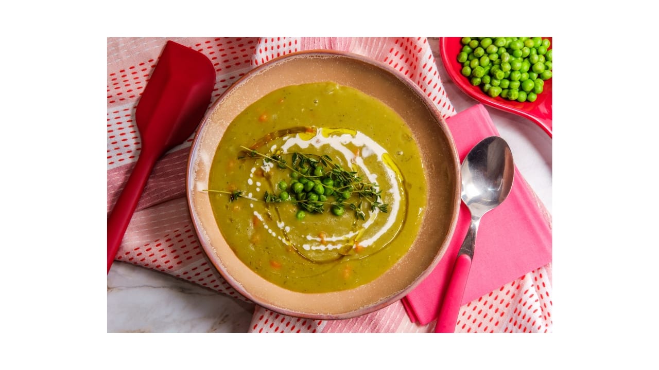 A bowl of British split pea soup with drizzle of cream and olive oil garnished with fresh thyme sitting on a table ready to be enjoyed..