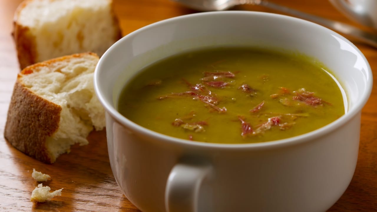 A bowl of classic American green split pea soup made with smoked pork ham hocks, served with crusty bread.